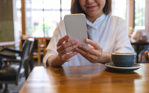 Closeup image of a young woman holding and using mobile phone in coffee shop
