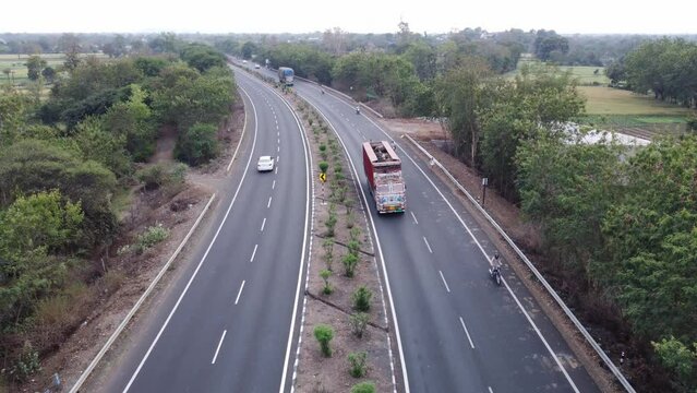 High angle shot of a generic new well maintained national highway of India with rural landscape of farmlands and lush green tree border with trucks and passenger vehicle movement