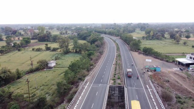 Drone aerial view of a generic looking well maintained national highway of India with rural landscape of farmlands and lush green trees passing over a dried up river