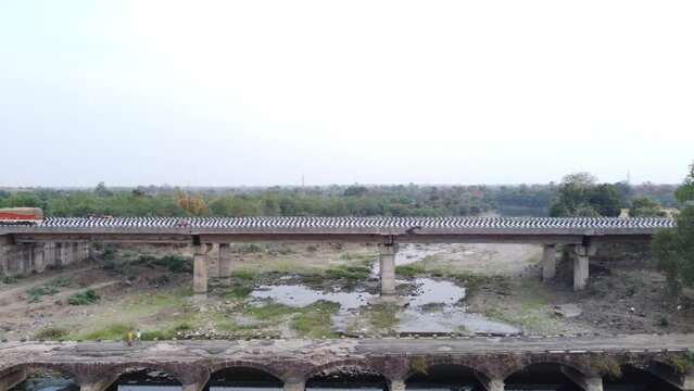 Drone charging towards a demolished old bridge in foreground with a newly built 6 lane highway bridge in background over a typical dried up river basin in the mainland Indian rural terrain