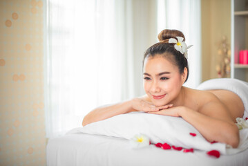 Surrounded by the delicate fragrance of roses the beautiful asian woman seemed lost in a world of her own free from stress and worries on the bed strewn with roses in spa room.