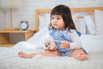 Fototapeta premium Little girl's eyes lit up with joy as she holding her furry friend close to her heart on the bed in the bedroom while looking sideway.