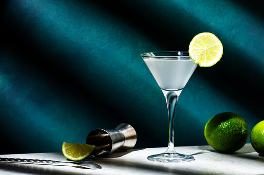 Vodka gimlet alcoholic cocktail with vodka, sugar syrup, lime juice and ice in martini glass, dark green background, hard light and shadow pattern