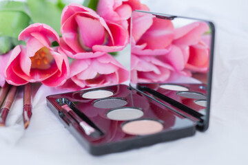 Pink tulips, eye shadow palette with mirror, brushes on white background, women makeup cosmetics set