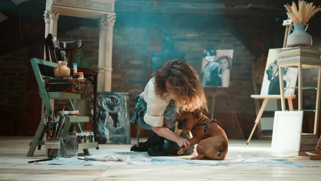Artist girl takes her dog's paw print on a canvas in her studio