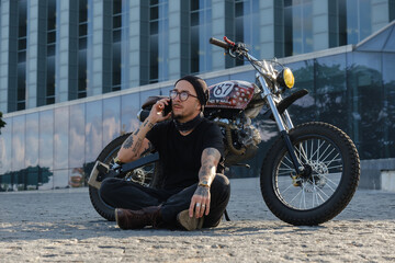 Fototapeta na wymiar Shot of trendy motorcyclist with vintage oldfashioned bike against background of city building.