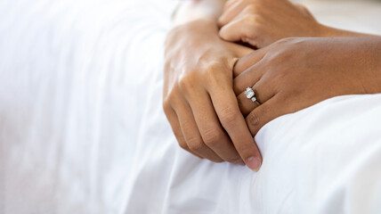 Close up hand of husband and wife holding together on the bed with wedding diamond ring on her finger for love, sensual, romance and intimacy relation concept