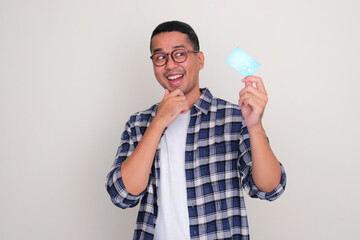 Adult Asian man smiling happy when looking to credit card that he hold