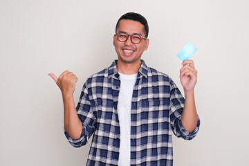 Adult Asian man smiling and pointing to the right side while holding credit card