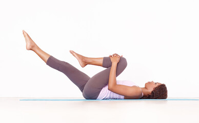 Yoga, leg stretch and black woman in studio on a fitness and workout mat for training. Isolated, white background and African female person lying on the ground with sport stretching for wellness