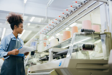 Obraz premium American Curly Hair Designer Half Body Photo in a sewing factory Walking and inspecting the weaving machines and multi-colored threads. wearing uniform holding a list of products