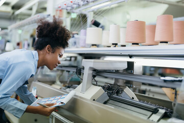 Obraz premium American seamstress designer with curly hair He was checking the weaving machine and the sewing thread attentively. wearing a uniform and carrying a catalog in the weaving industry