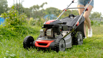 a girl with a lawn mower mows the lawn