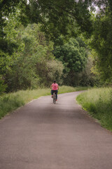 A woman in comfortable pink clothes riding a mountain bike on a road with trees on the side.