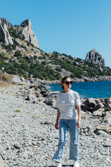 a woman in jeans stands on the seashore by the rocks beach nature