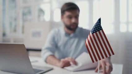Male office employee working with documents, typing on laptop, USA flag on desk - Powered by Adobe