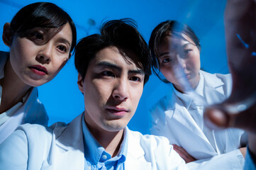 Three Asian researchers looking into a test tube.
Taken from below