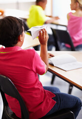 Bully, boy child with paper plane in classroom and sitting at his desk with behavior problem....