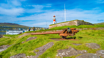 Fototapeta na wymiar Torshavn, Faroe Islands - Lighthouse, old military fortress Skansin with cannons, WWII guns and tourists in the modern capital Torshavn of Faroe islands