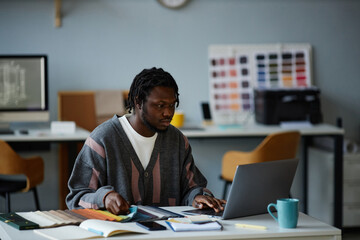African American designer working on laptop with project online while sitting at his workplace in...