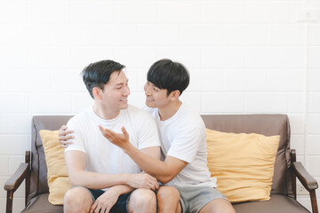 Happy Asian gay couple hug together on sofa. Asian LGBT couple embracing together at home. Diversity of LGBT relationships. A gay couple concept. LGBT multi relationship.