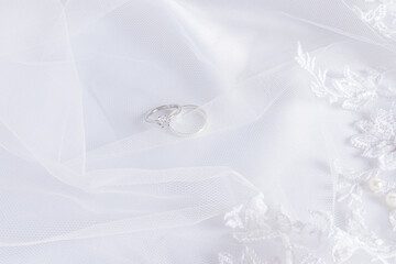 Top view of two diamond platinum engagement rings on a white chic satin background with soft waves and pearls. Wedding background.