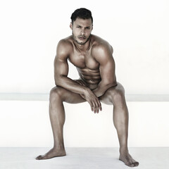 Nude, body and man in portrait isolated on a wall background for health, fitness and wellness. Naked, strong and face of a sexy male model sitting with muscles for power, sports and exercise results - obrazy, fototapety, plakaty