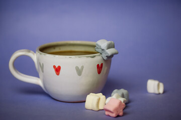 A cup of coffee, cocoa, chocolate with hearts on a lilac violet background. Marshmallows on a table. Cozy still life with hot drink made with love, sweets. February 14, Happy Valentines Day concept. 
