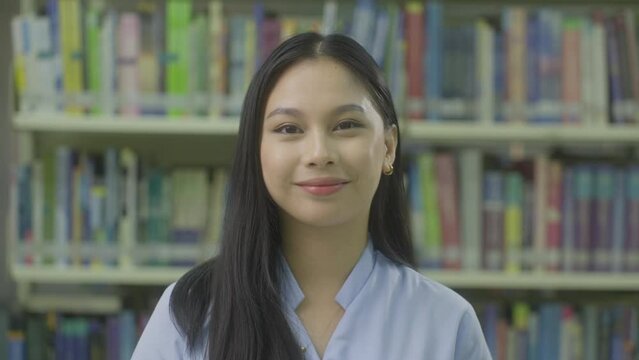 Young Female College Student Smiling At the Camera With Library Books In The Background. - close up