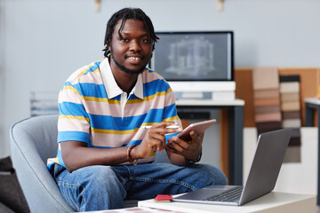 Portrait of African American designer smiling at camera while using tablet pc in his work