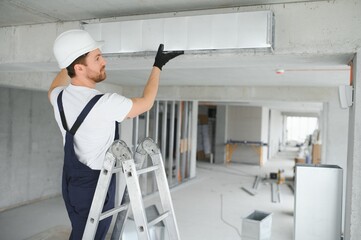 Professional HVAC Worker on a Aluminium Scaffolding Installing Air Duct Inside Newly Built...