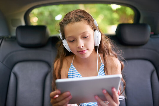 Technology, young girl in car with tablet and headphones while travelling. Social media or streaming, internet connectivity and child on road trip on vacation in vehicle with digital or mobile device