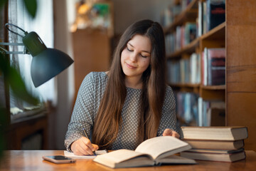 Young brunette student girl prepare for classes in library. Confident woman sitting at the table and writing notes for research report, educational concept