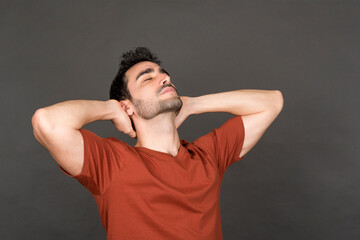 Relaxed young man with hands behind head in studio portrait.