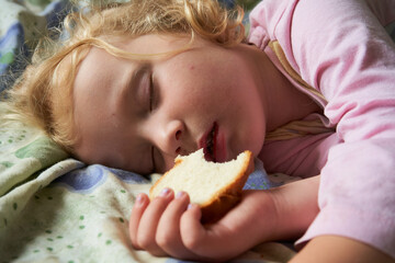 a child is sleeping with a piece of bread,a hungry and tired little girl fell asleep on the bed