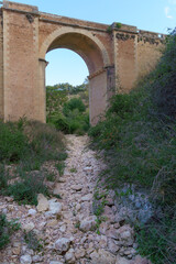 This photo shows a dry river bed in the foreground, with a bridge passing overhead. The scene captures the effects of climate change and drought, with the barren landscape of the riverbed emphasizing 