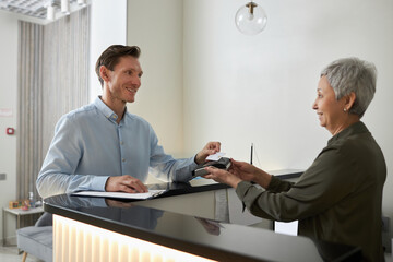 Portrait of smiling elegant man paying in medical clinic via NFC technology, copy space