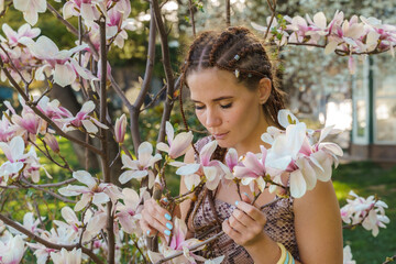 Magnolia flowers. Happy woman enjoys by blooming magnolia tree and sniffs it flowers with closed eyes in spring garden. Portrait.