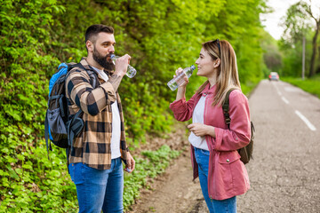 Naklejka premium Happy couple hiking in nature and drinking water. Couple enjoying their vacation.