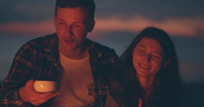 Social distancing together. Pretty young couple playing drinking tea or coffee near the bonfire at night. two lovers spending time at nature far away from croudy place. Safety way to spend free time