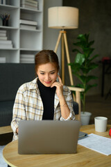 Portrait of charming young woman freelancer working online, answering client on laptop computer