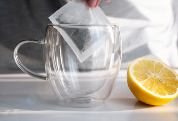 A girl's hand puts a tea bag in a cup. Black tea with lemon in the morning. Close-up. Selective...