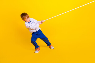 Profile side full length photo of little schoolkid boy pull heavy rope tug war game isolated on...