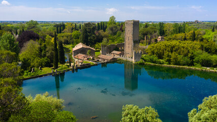 Fototapeta premium Aerial view of the ruins of the castle and tower located in the garden of Ninfa, near Latina, Italy. The park is an Italian natural monument and contains a lake and a river. It is empty.