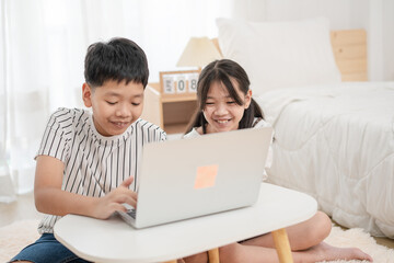 Asian brother and sister using laptop to learn at home