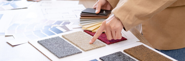 Female interior designer choosing color of wood and carpet material  with drawing construction plan...