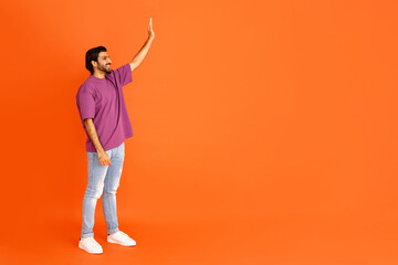 Fototapeta na wymiar Cheerful eastern guy waving at copy space, orange background