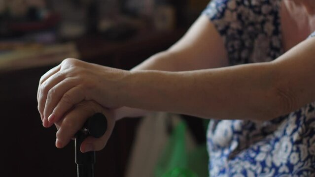 hands of an elderly woman holding a cane for walking while sitting inside. leg diseases in old age, chronic diseases,. be healthy concept