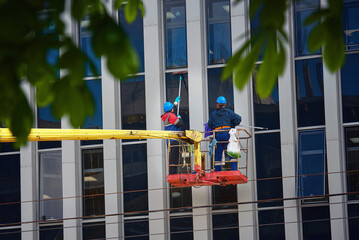 Window washing of high-rise office building in crane bucket. Workers team washing glasses windows at height in lifting platform. Window cleaner, building exterior wet wash. Clean service team © Tricky Shark
