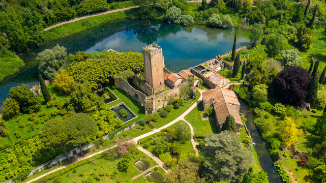 Aerial view of the ruins of the castle and tower located in the garden of Ninfa, near Latina, Italy. The park is an Italian natural monument and contains a lake and a river. It is empty.